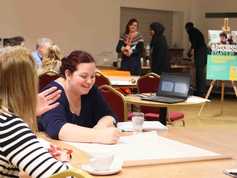 A group of people sitting around a table, smiling and discussing ideas during a workshop or meeting.