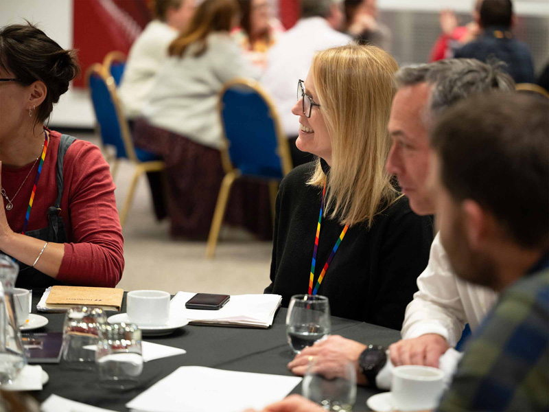 A woman smiling and listening attentively while sitting at a table with a group in a workshop.