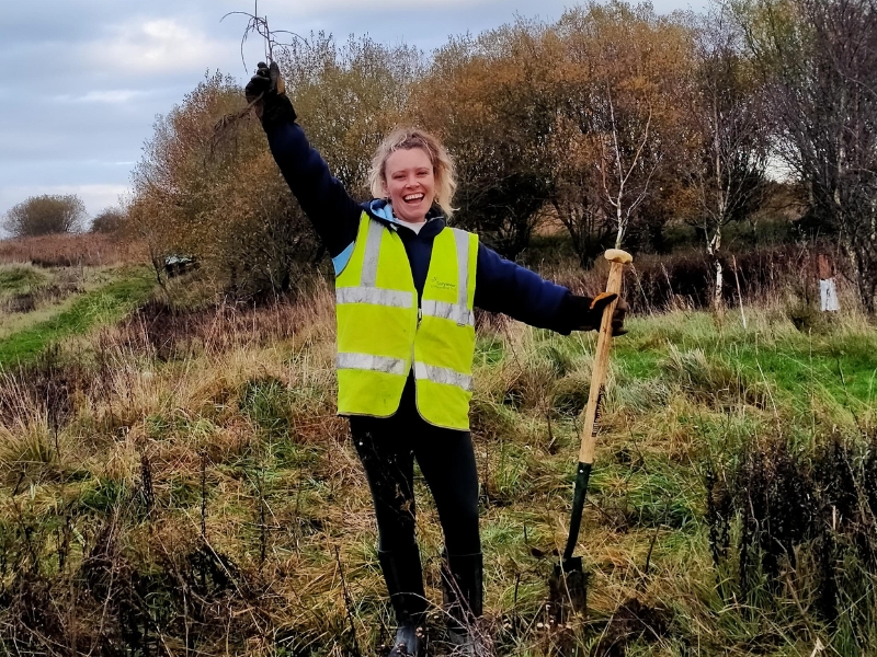 Photograph of a woman in a field, arm raised holding a space and smiling.