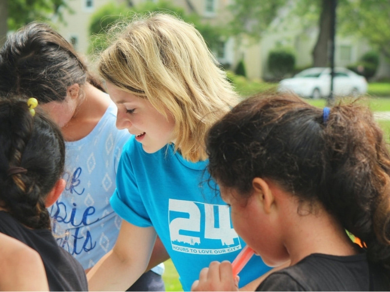 Photograph of a young woman, smiling, stood amongst children