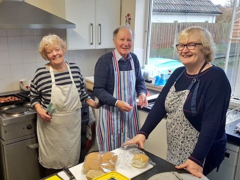 Photograph of a group of people preparing food in a kitchen, smiling at the camera