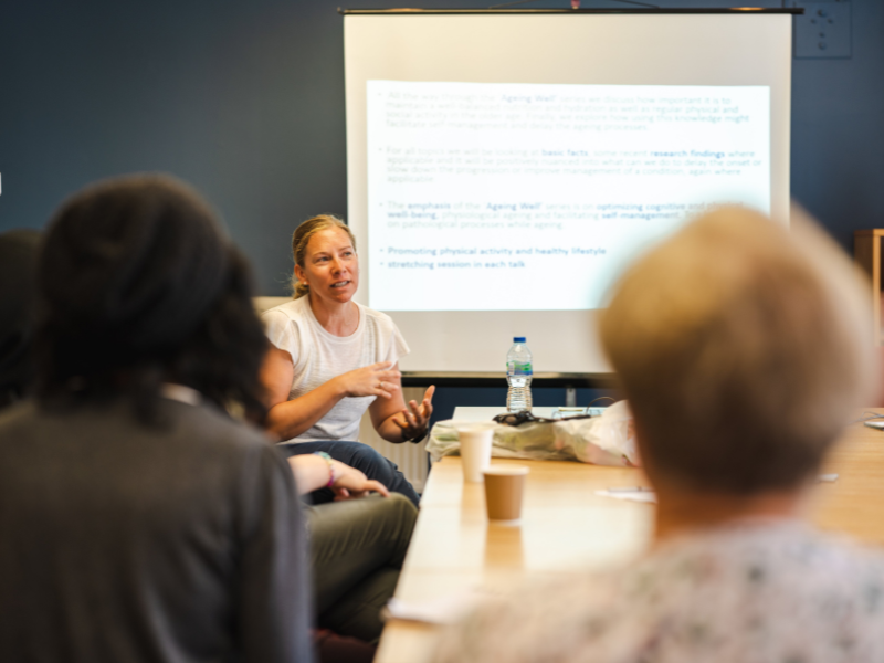 Photograph of three women sat at a table having a discussion with a presentation in the background.