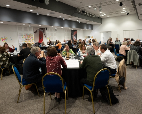 Photograph of a room full of people having a discussion at a conference.