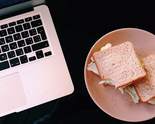 A top-down picture of an open laptop with a plate of sandwiches next to it.