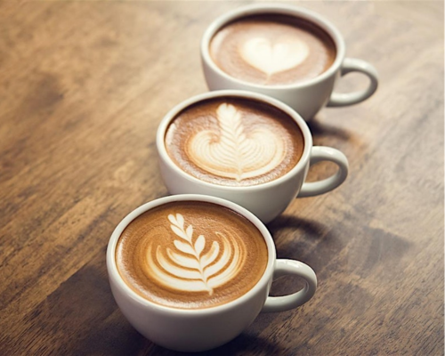 An image of three coffee cups on a wooden worktop. Coffees feature feathered latte art.