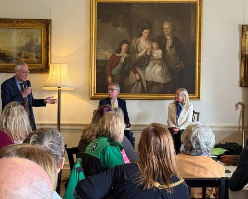 Photograph of attendees at an event, backs to the camera, looking at the speakers